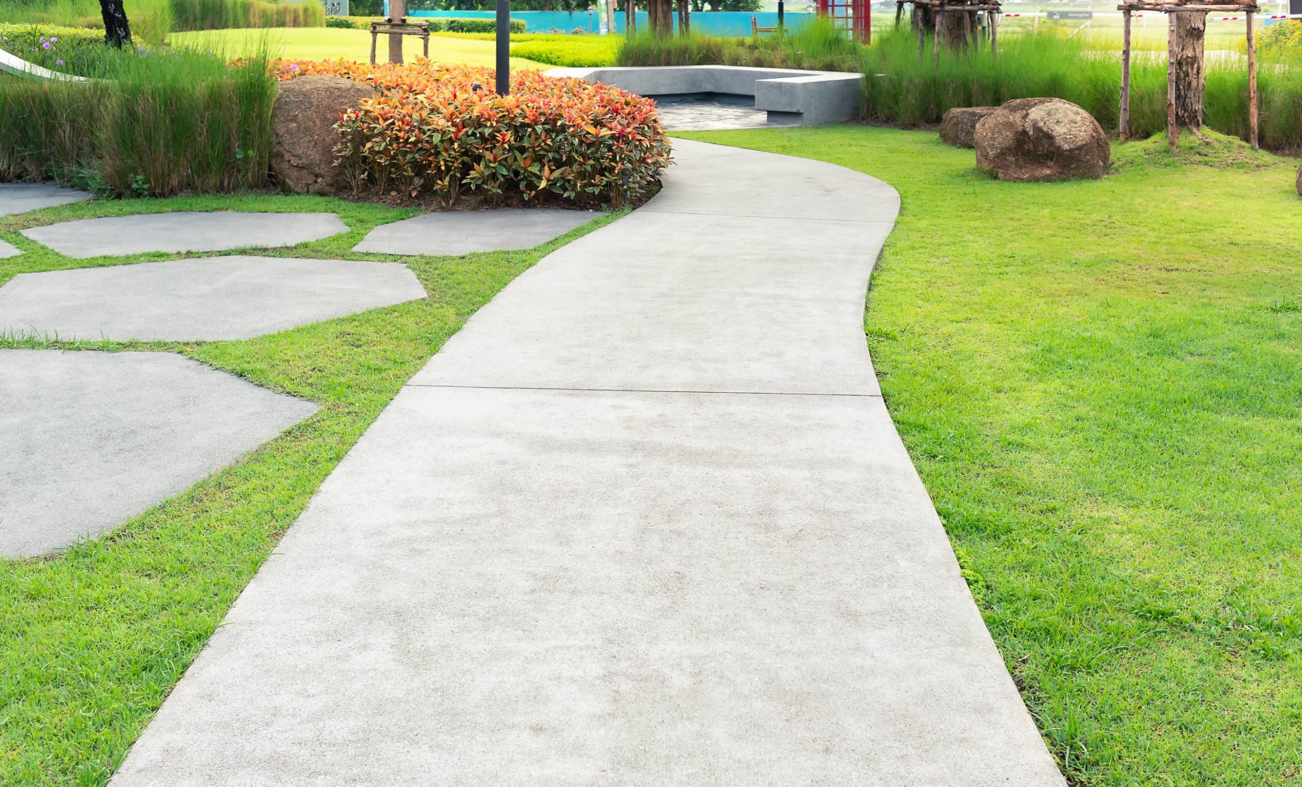 This is a picture of a concrete walkway with some decorative concrete paths and concrete bench in a garden.